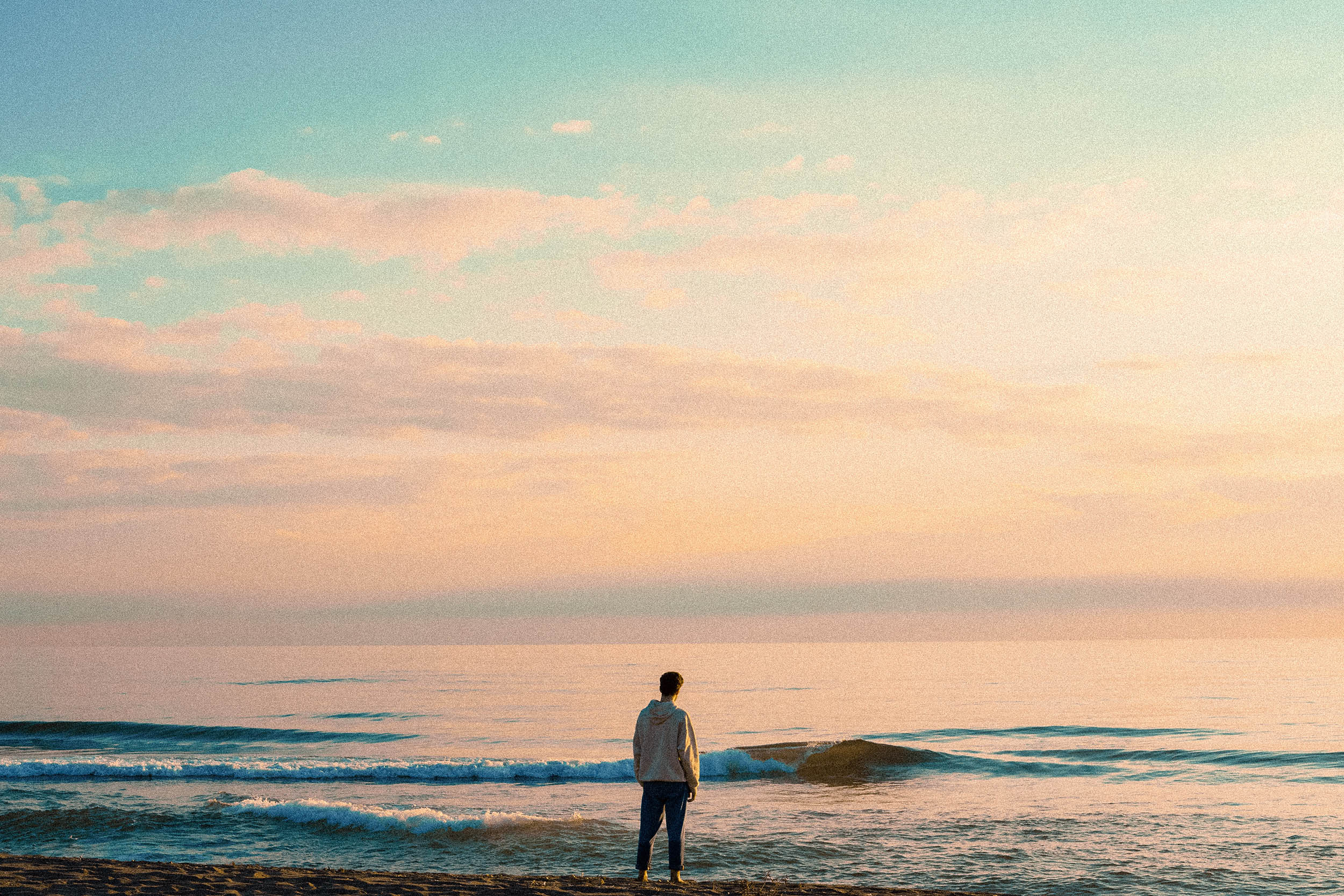 Young man standing on the beach at sunset